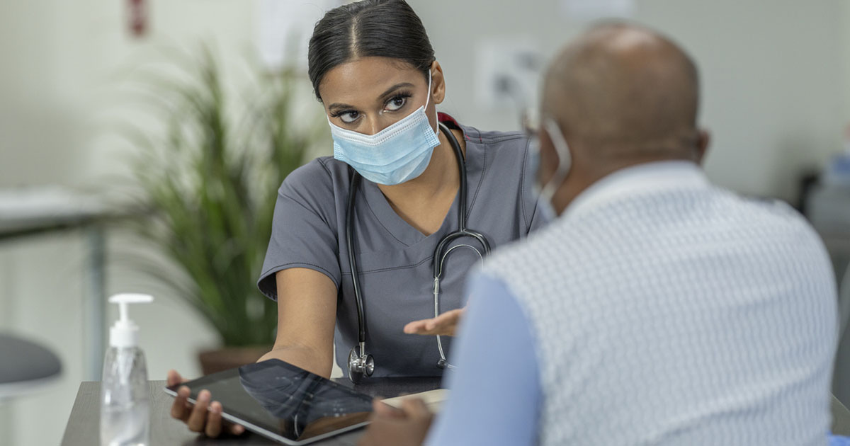 A senior patient and a female doctor meet in a medical clinic while wearing protective face masks to avoid the transfer of germs.