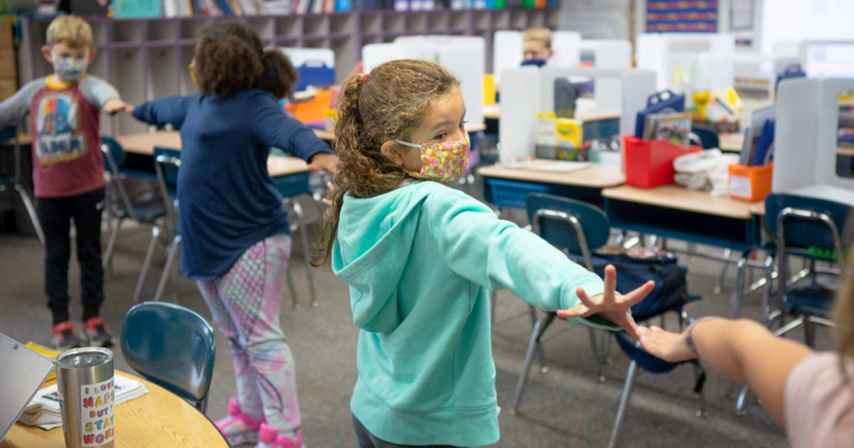 Second-grade students create distance between each other using their arms as they line up to go outside.