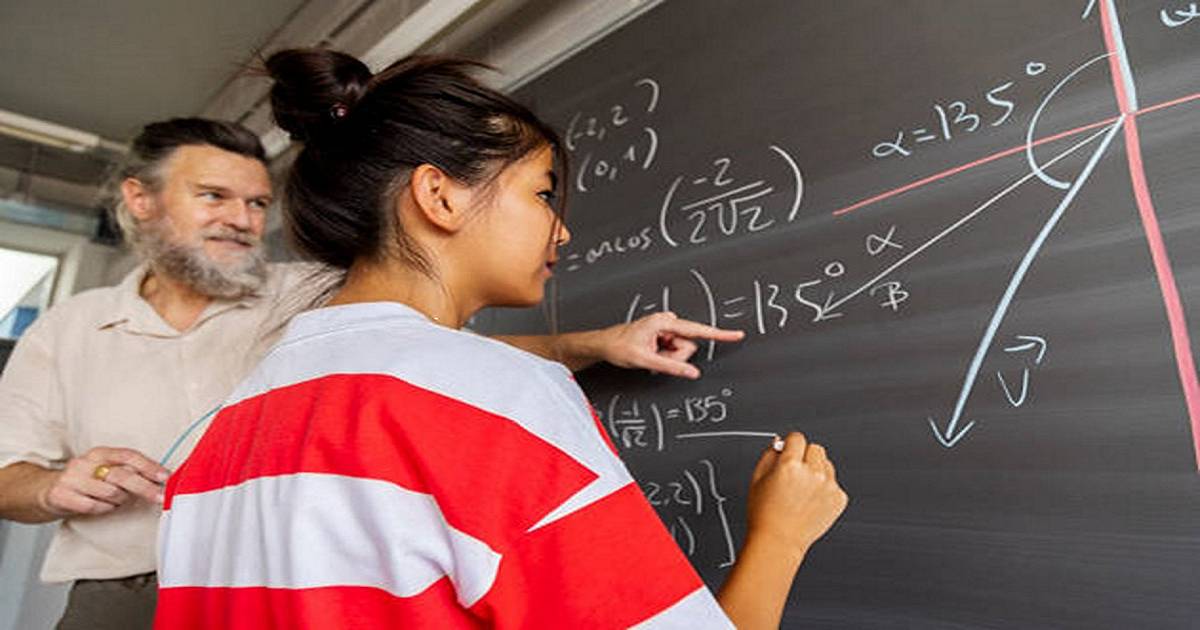 Caucasian male high school mathematics teacher explains blackboard exercise to female Asian student