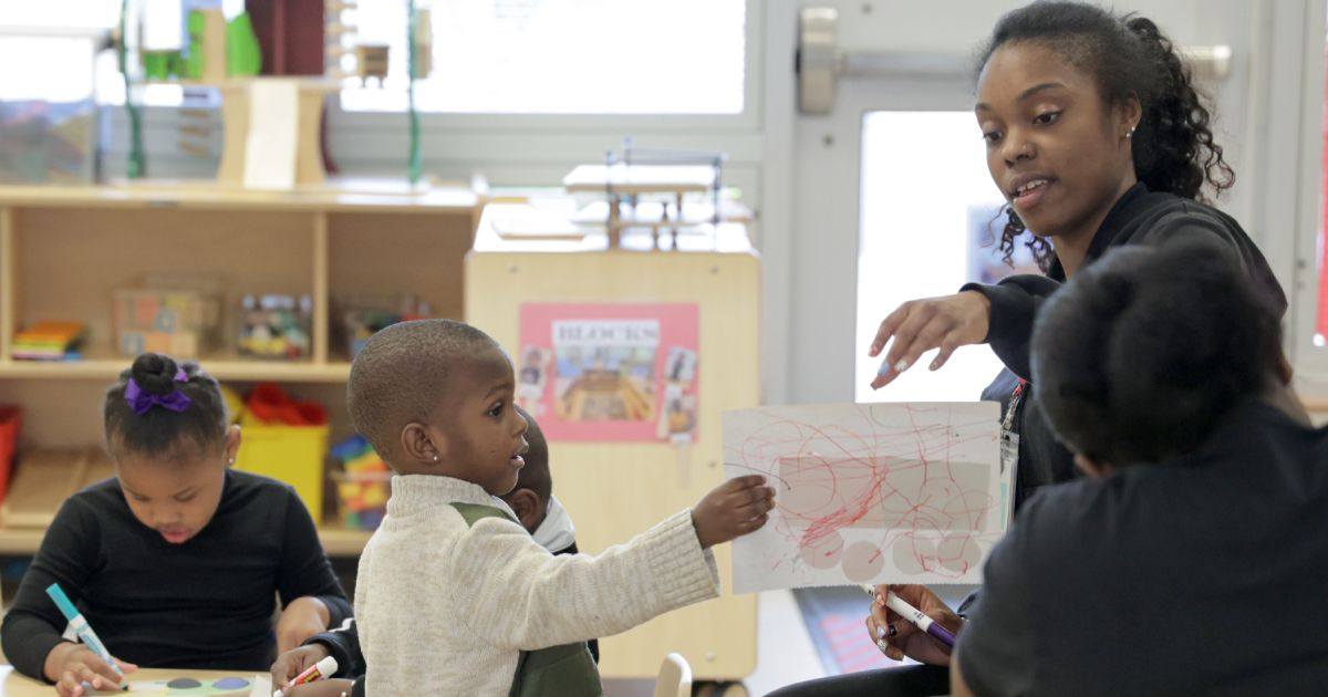 Preschool children sitting on the floor in a circle with an educator talking to them.