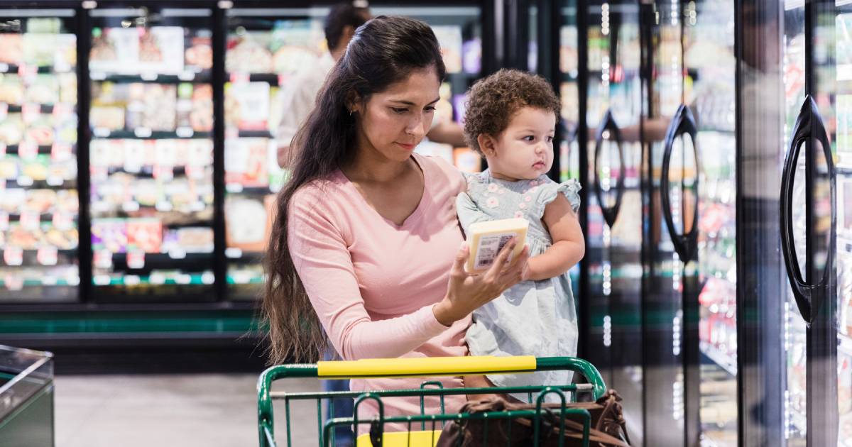 A mother holding a baby looking at food items in a grocery store