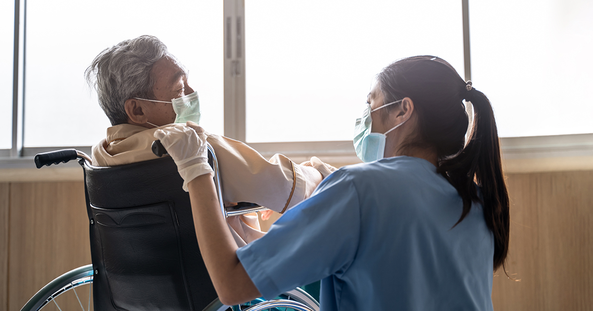 Asian nurse taking care of mature male patient sitting on wheelchair in hospital