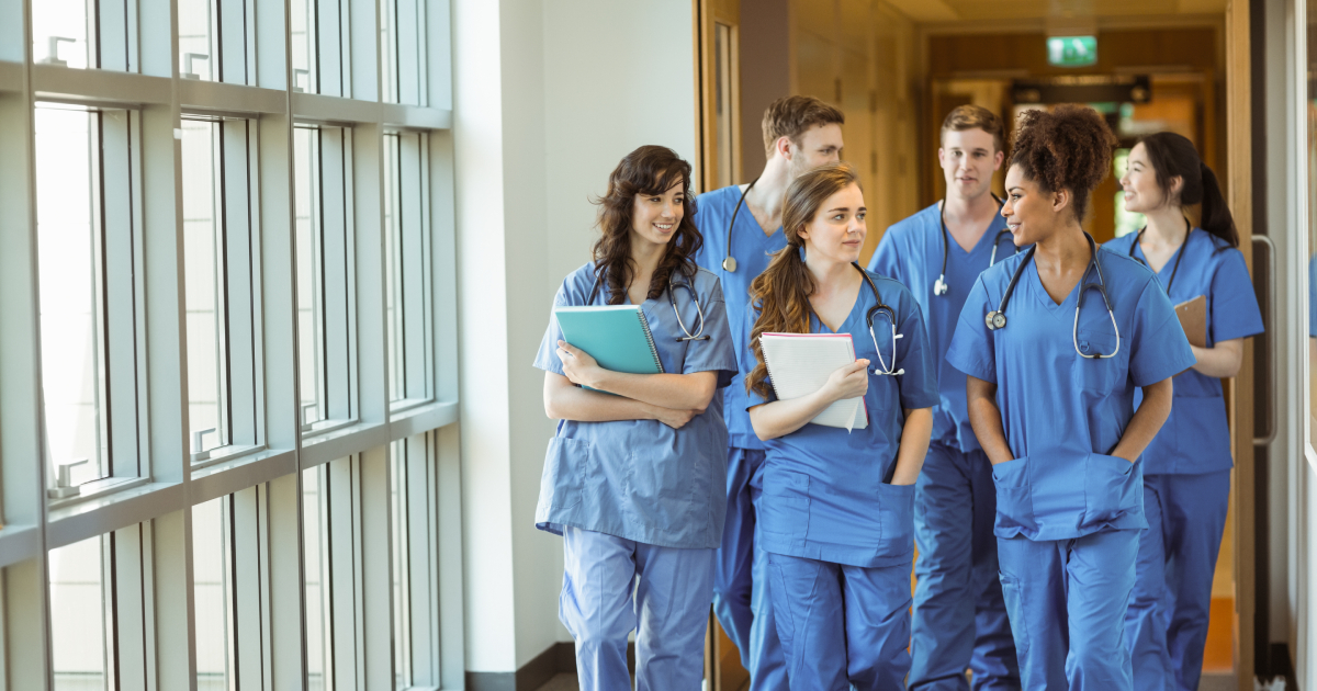 A group of medical students in scrubs walk down a hallway. 