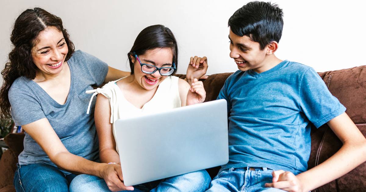 Family of mom and young teen or preteen boy and girl sitting on a couch smiling and looking at a computer screen