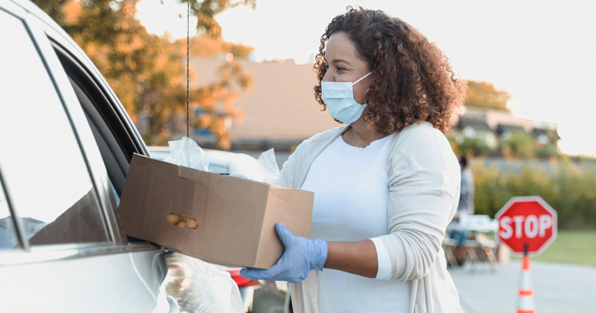 Woman with a boxed meal giving to a motorist in line for free meals