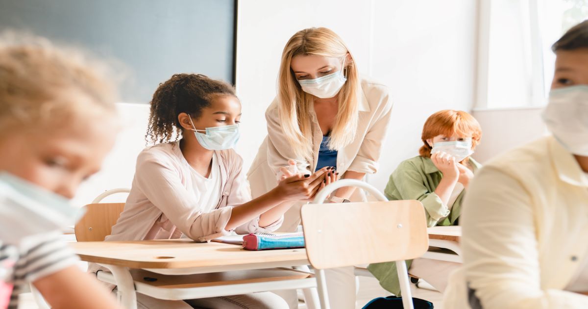 Teacher helping student in a classroom during COVID