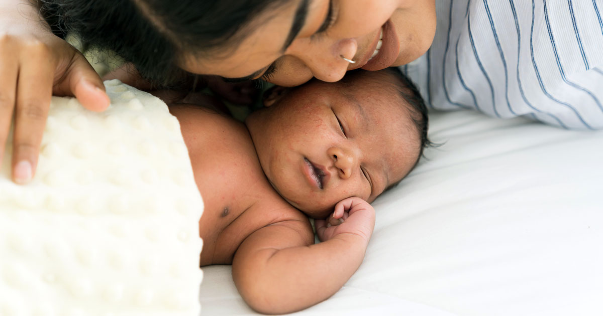 Top view of mother kissing her newborn baby on a bed. 