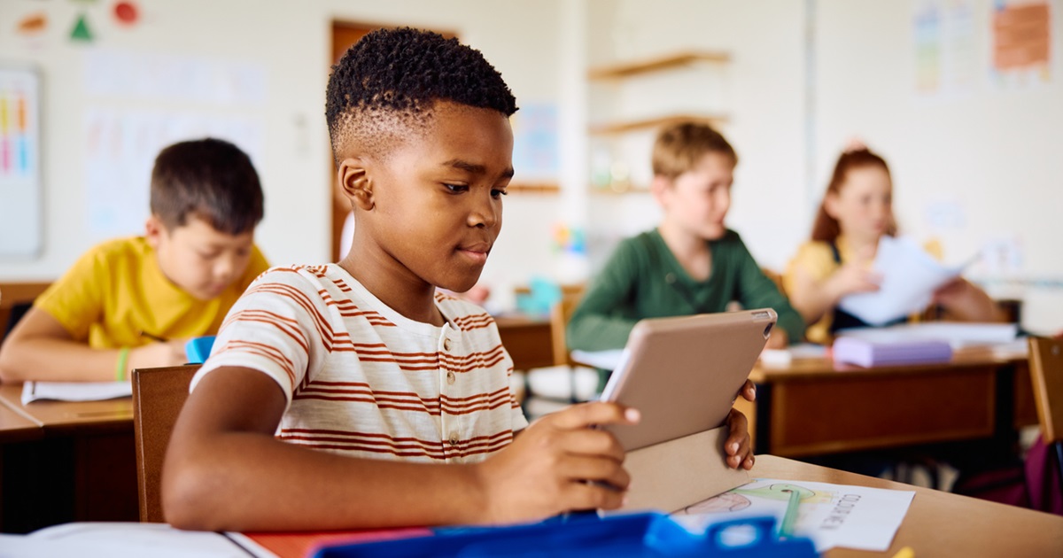 Schoolboy sitting at desk, watching tutorial online and learning with digital tablet in classroom