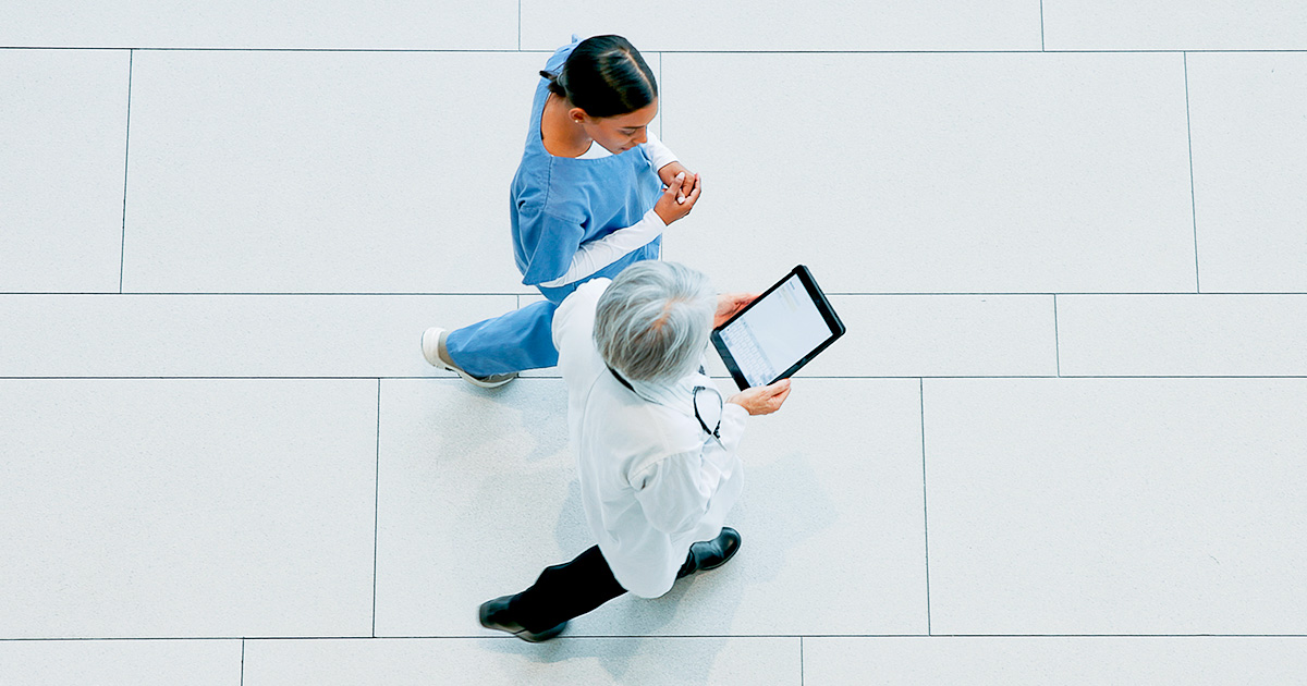 Overhead view of a doctor and nurse walking through a health care facility while reviewing information on a tablet.
