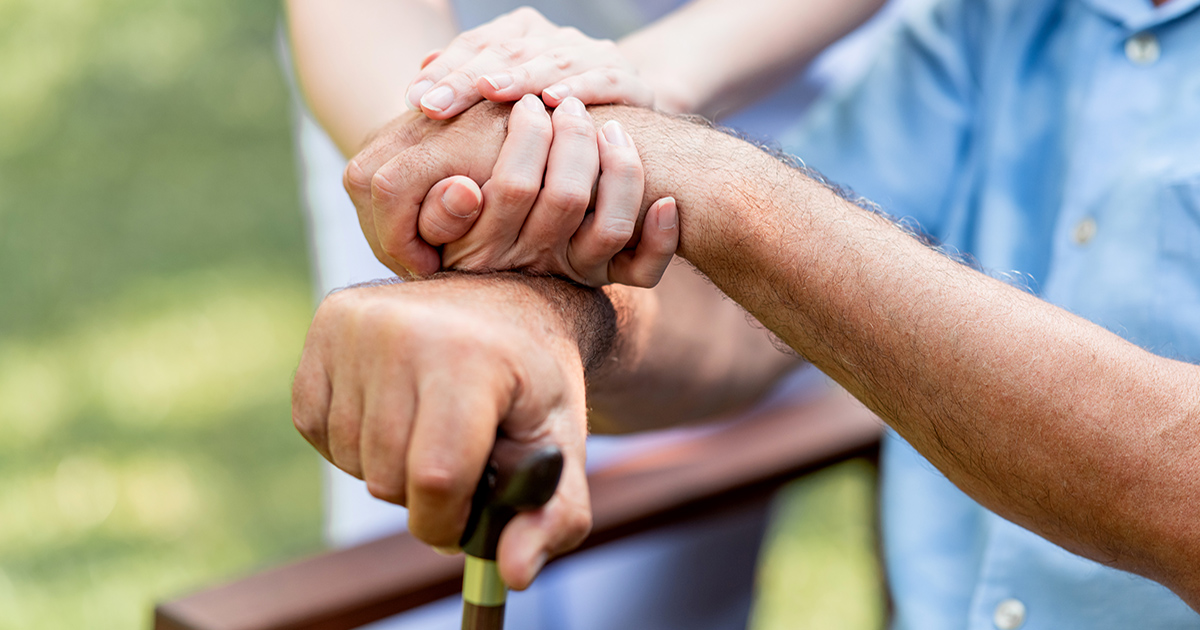 Caring nurse helping senior man sitting on bench in gaden. Asian woman, caucasian man. Holding hands with cane, close up.