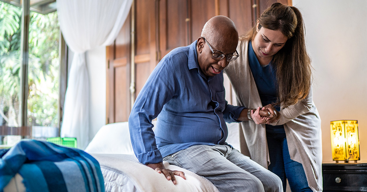 A medical professional helps a sitting elderly  man to stand up