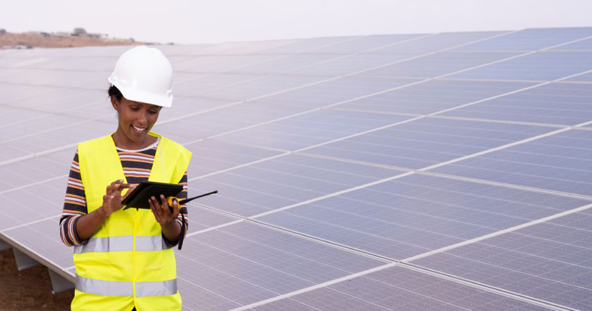 Woman in hardhat working on a tablet in front of solar panels