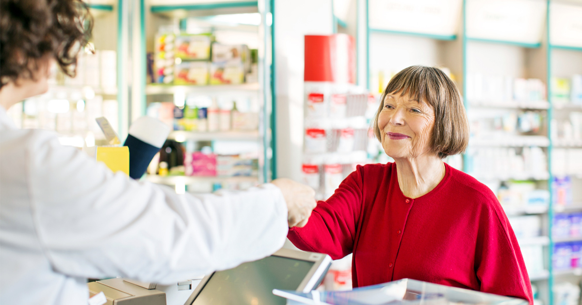 An elderly woman purchases prescription drugs at a pharmacy counter.