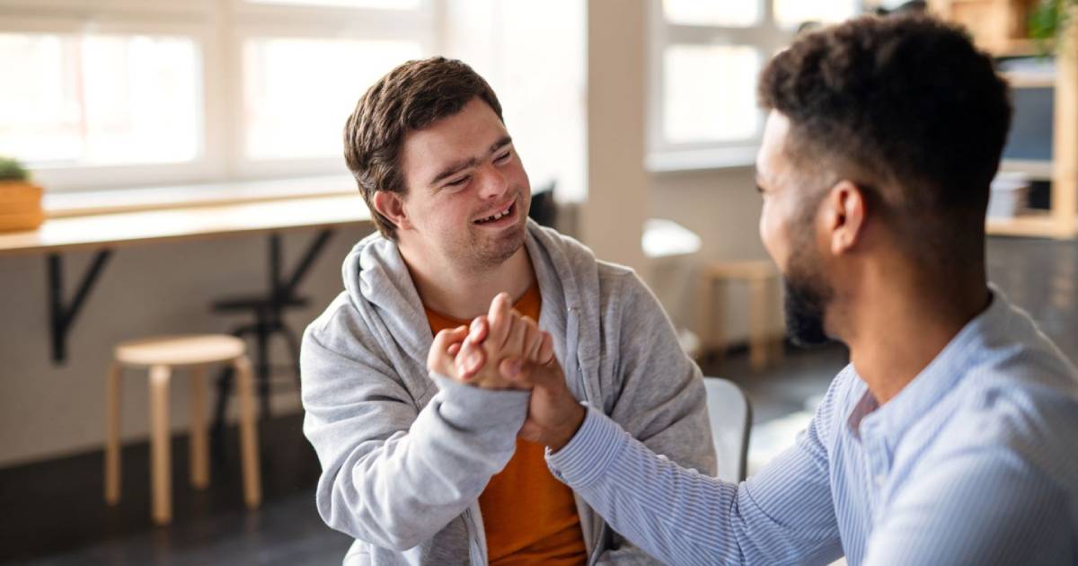 A smiling young man with Down Syndrome shakes another man's hand.