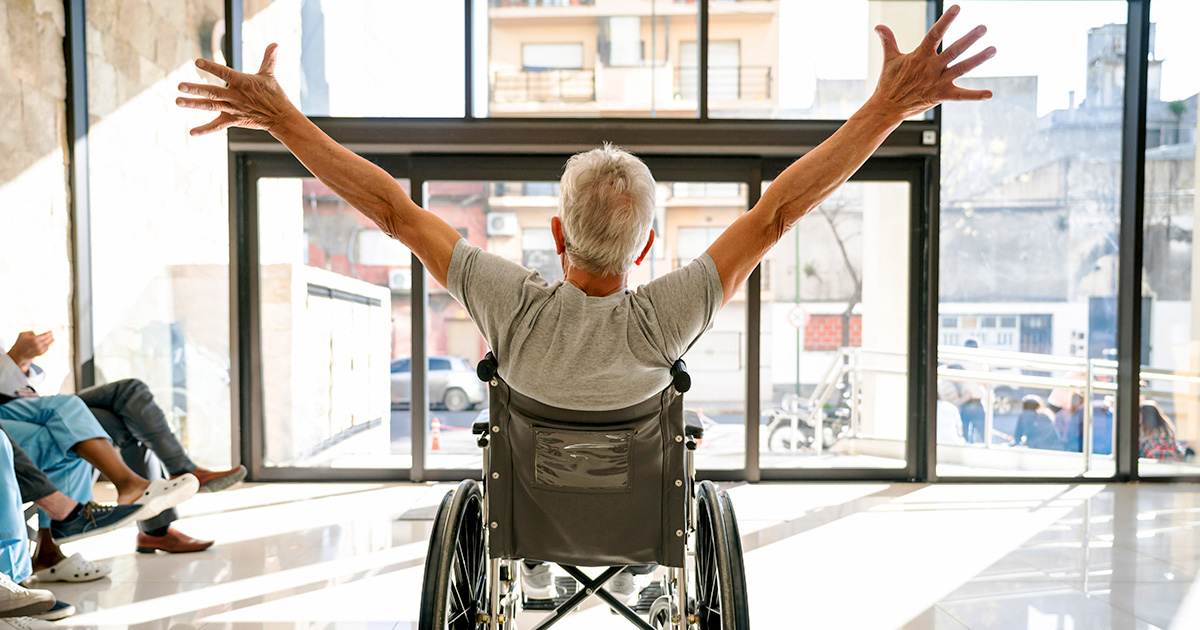 A senior patient leaving the clinic on a wheelchair with his arm up.