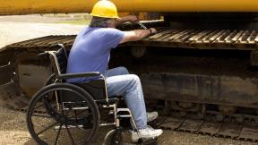 Worker with a hard hat in a wheelchair works on a construction vehicle