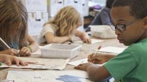 Three elementary students writing in school setting